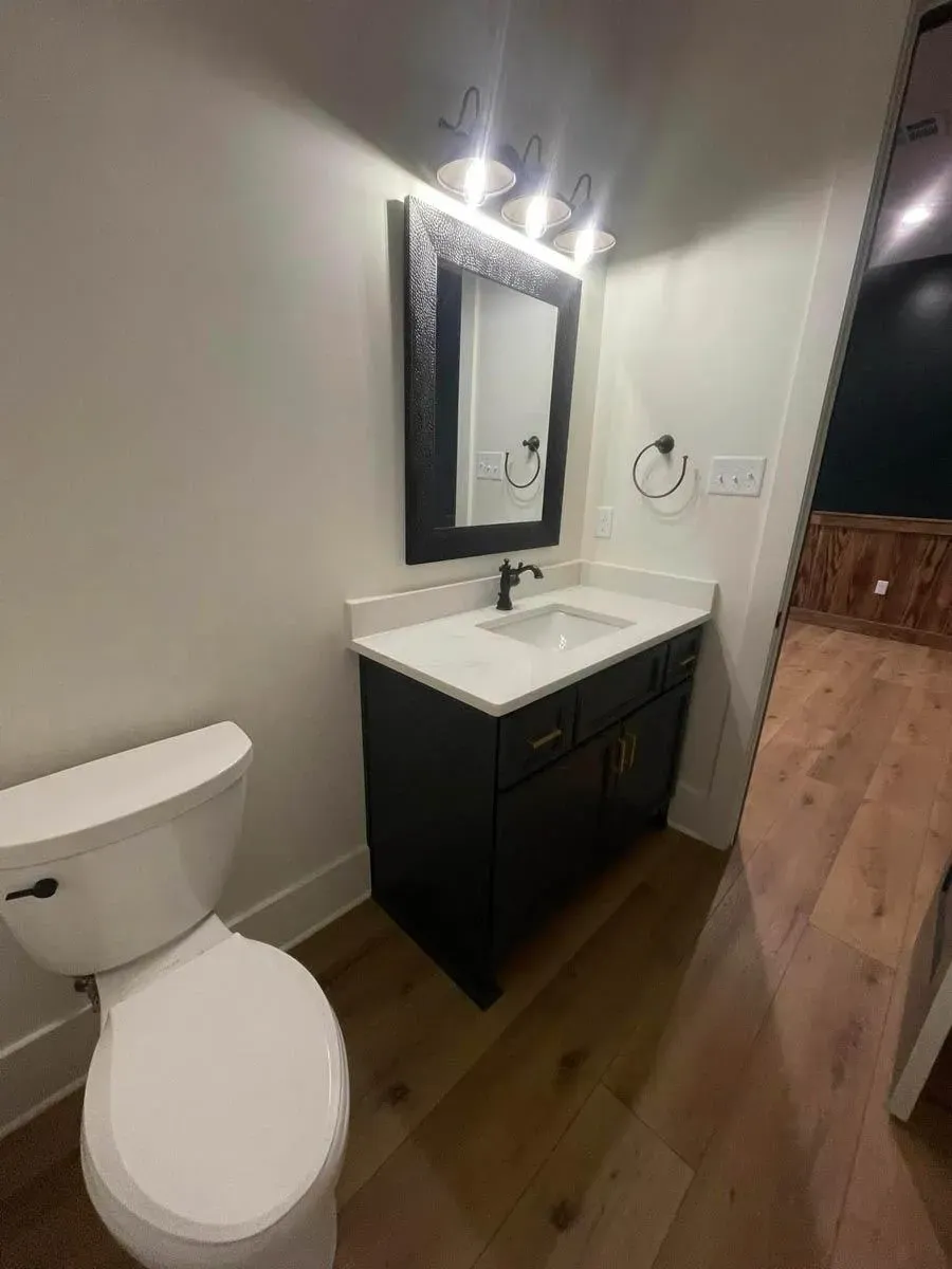 Game room half bath with a dark green vanity, a black-framed mirror and wood-look floors