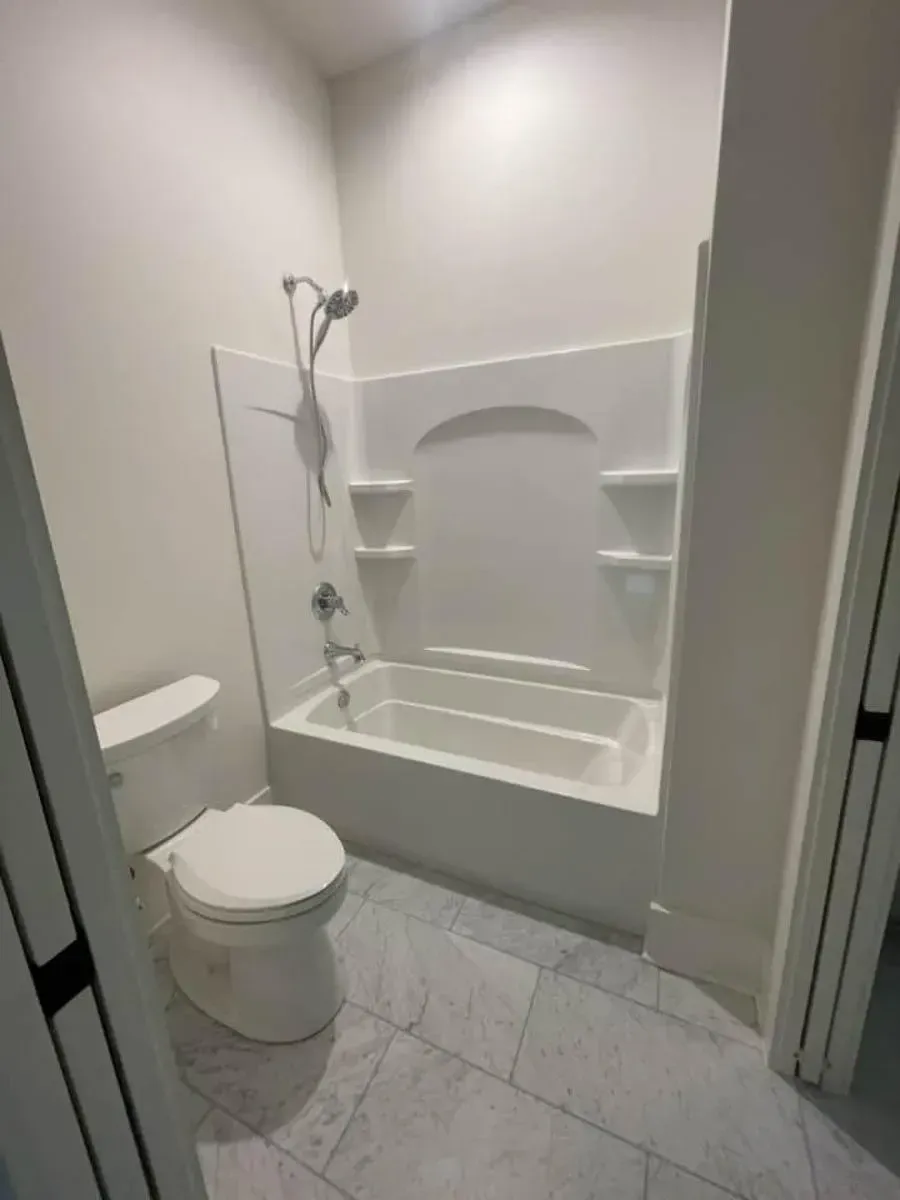 Shared tub-and-toilet room of the Jack and Jill bath with a white tub-shower and a handheld shower head
