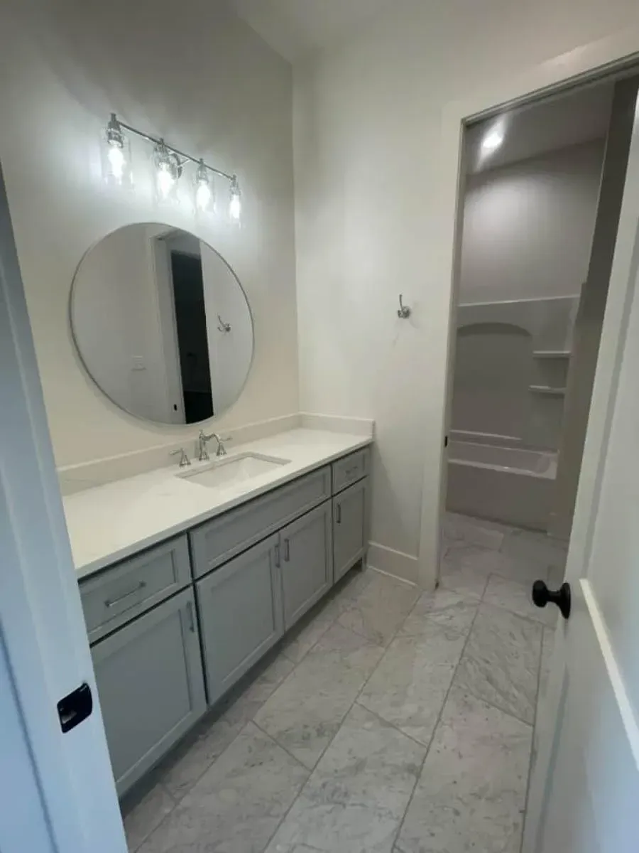 Jack and Jill vanity with a gray shaker cabinet, quartz top, round mirror and a door to the shared tub room