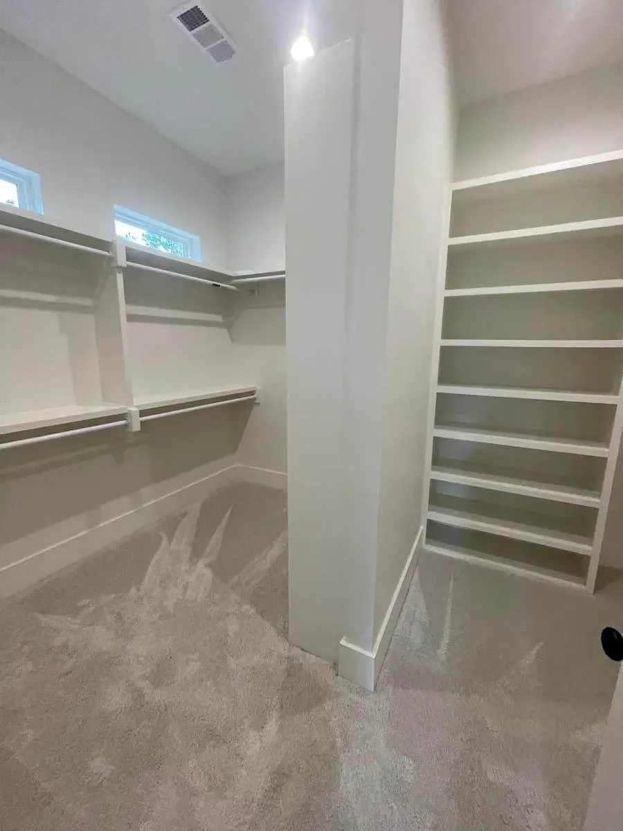 Primary walk-in closet with white shelving on every wall, hanging rods and high windows