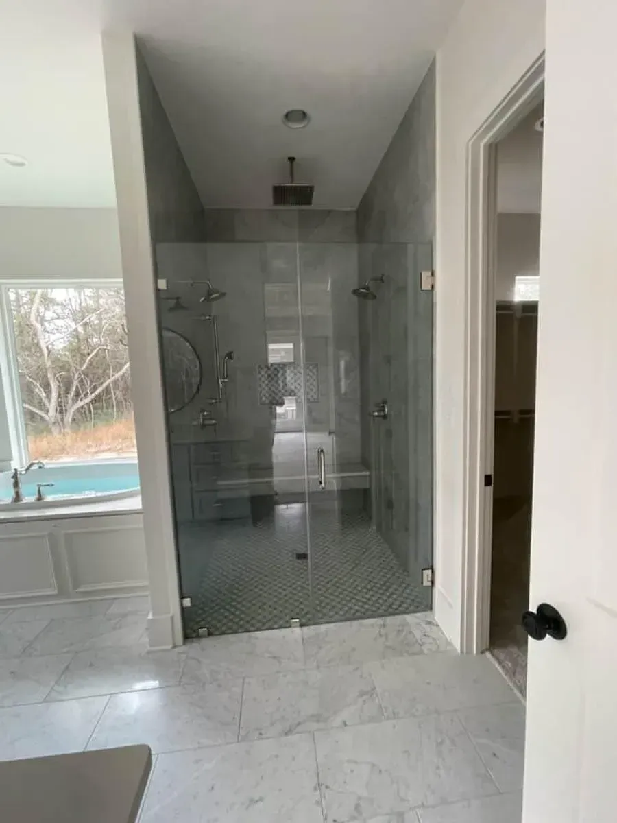 Frameless glass shower in the primary bath beside the soaking tub, with marble-look tile floors
