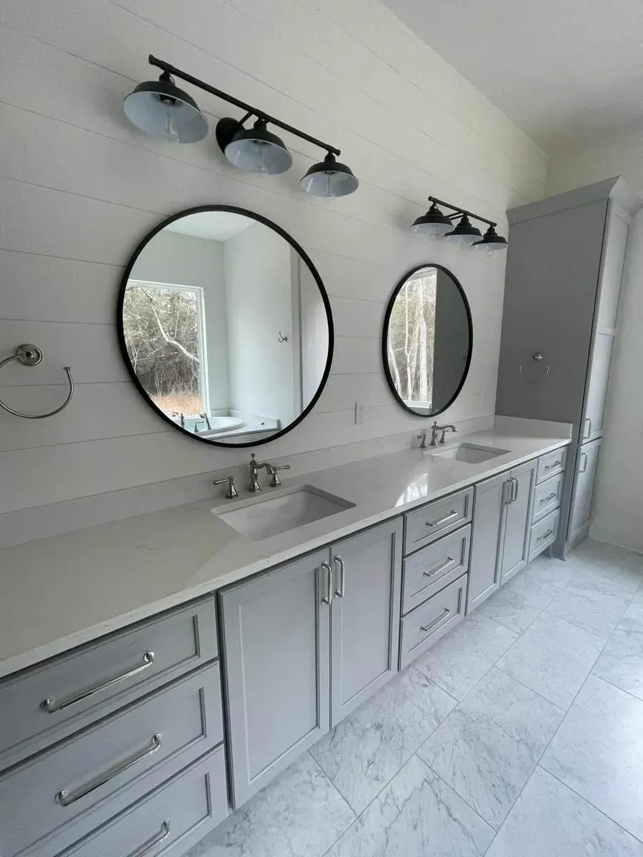 Primary bath double vanity in gray shaker cabinetry with two undermount sinks, round black mirrors and black barn-style sconces