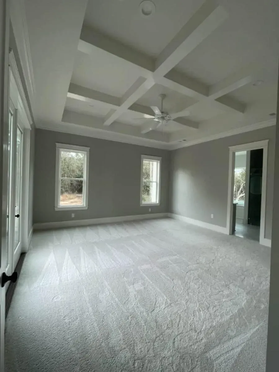 Primary bedroom with a coffered tray ceiling, ceiling fan, carpet and windows and a door to the backyard