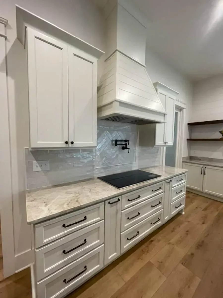 Range wall with white shaker cabinets, a white plaster hood, a cooktop, a pot filler and a white tile backsplash