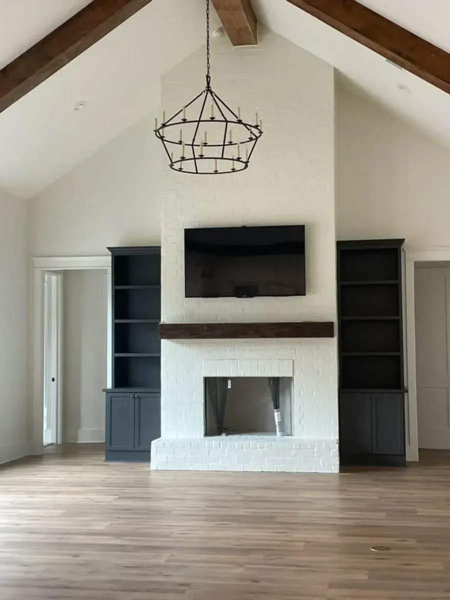 Fireplace wall with painted white brick, a wood mantel, a mounted television and dark built-in cabinets on both sides under a beamed vaulted ceiling
