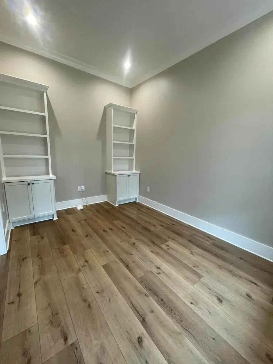 Study near the foyer with white built-in shelving units on either side of the room and wide-plank oak flooring