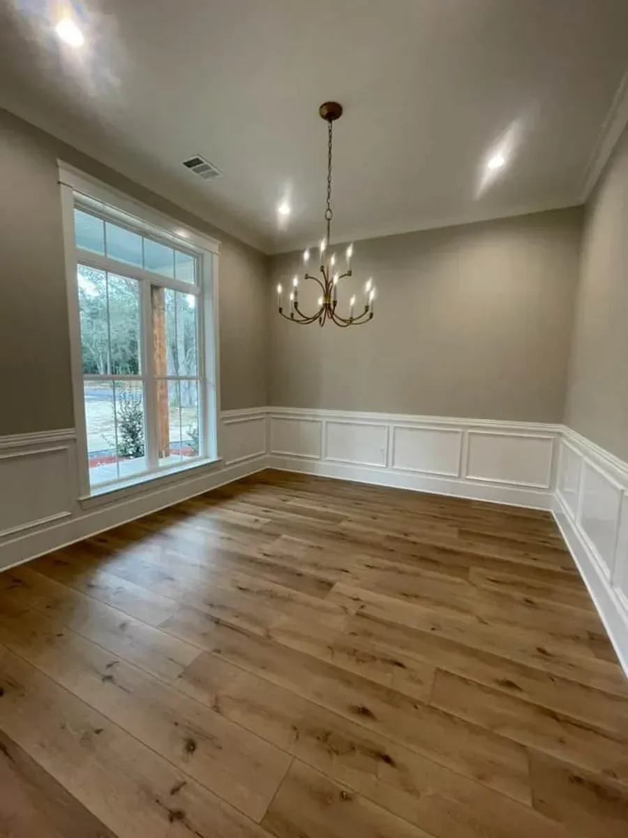 Formal dining room with white wainscoting, a brass chandelier, wide-plank oak floors and a tall window