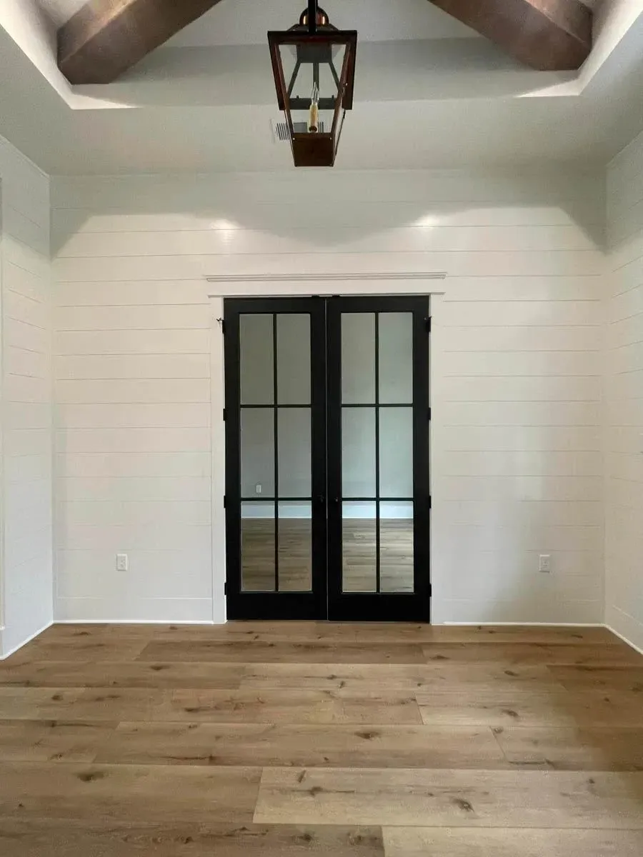 Foyer in the finished build with shiplap walls, a beamed ceiling, a lantern pendant and black glass double doors