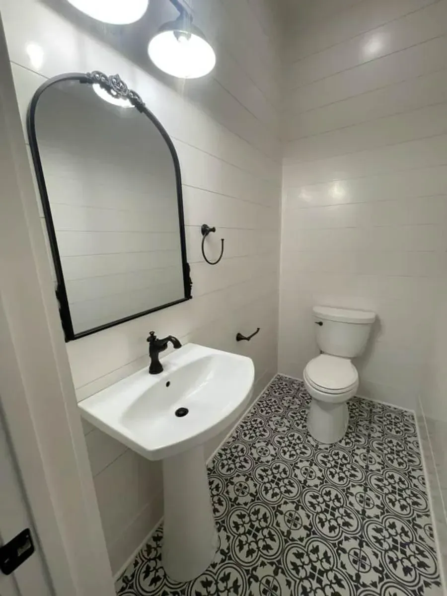 Powder room with a white pedestal sink, black arched mirror, white wall tile and black-and-white patterned floor tile