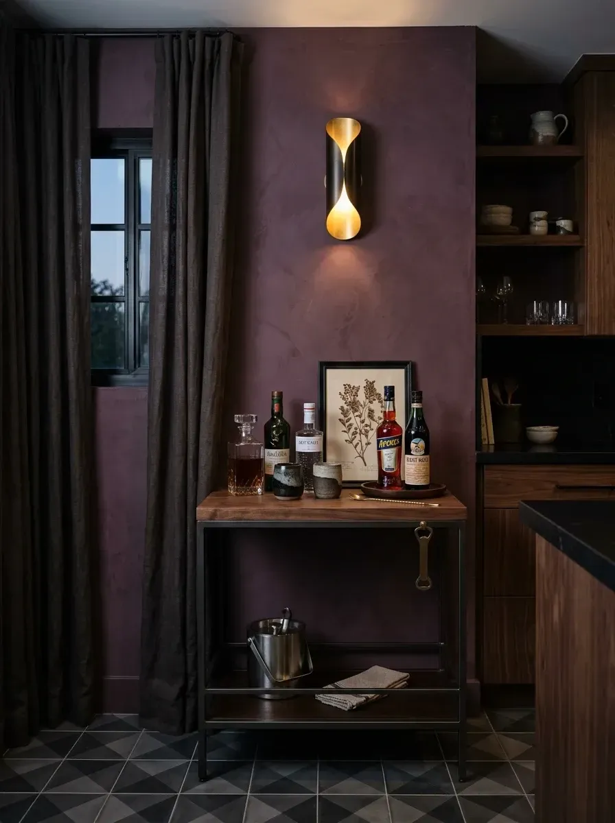 Plum limewash wall in a small bar nook with a sculptural brass sconce, industrial wood and metal bar cart and dark linen drapery