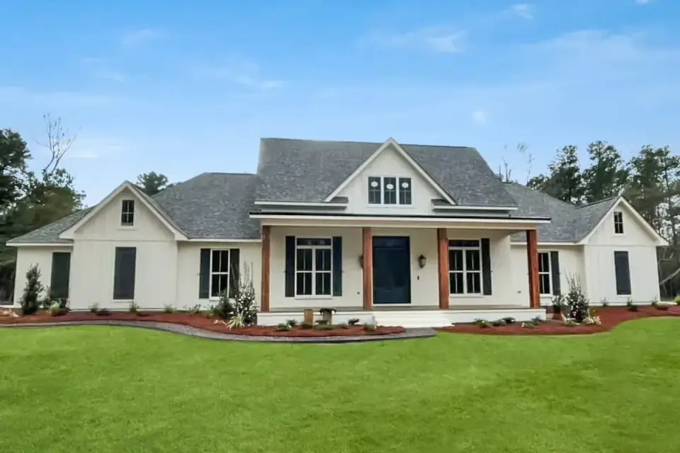 Finished build of modern farmhouse plan 185028PHD with white siding, three front gables, a center dormer, natural wood porch columns, black shutters and a dark front door