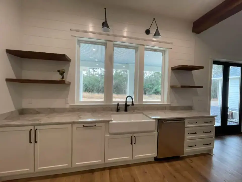 Kitchen sink wall with a white farmhouse sink, shiplap, open dark wood shelves, black swing-arm sconces and windows onto the rear porch