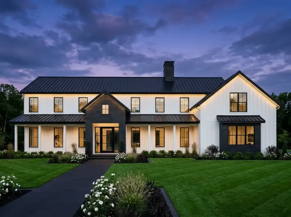 High-contrast modern farmhouse barndominium in crisp white siding against charcoal stone and black roofing with uplighting at dusk